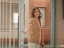 a woman in a tan jacket stands in front of a glass door that says kanald.com.tr