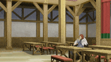 a man sits at a table in a room with wooden tables and benches