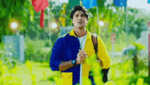 a man in a blue and yellow shirt is standing in a park holding a stick .