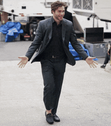 a man in a suit stands with his arms outstretched in front of a blue tarp