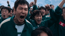 a group of people are screaming with their arms in the air while wearing green uniforms .