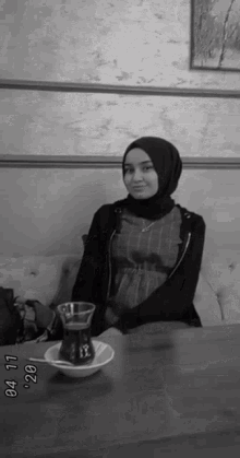 a woman in a hijab is sitting at a table with a cup of tea and a bowl of tea .
