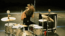 a person playing a drum set with a clock behind them