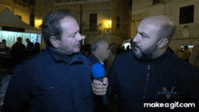 two men are talking to each other with a blue microphone in front of a crowd ..
