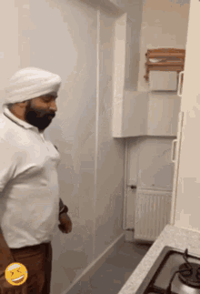 a man in a turban is standing in a kitchen with a smiley face on his pocket