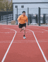 a man in an orange shirt and black shorts runs on a track