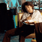 a man sits in a chair reading a book while a woman walks in the background