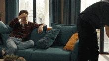 a man sits on a blue couch while another man stands behind him