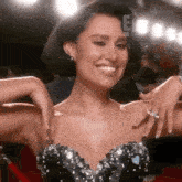 a woman in a black dress with rhinestones on it is smiling with her hands on her shoulder .