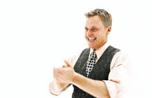a man in a vest and tie is smiling and clapping