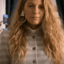 a woman with long blonde hair wearing hoop earrings and a striped jacket