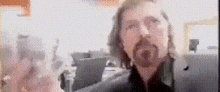 a man with long hair and a beard looks at the camera in a blurry photo .