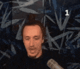 a man speaking into a microphone in front of a wall with the number 1 on it