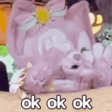 a purple teddy bear is laying on a bed with the words `` ok ok ok '' written below it .