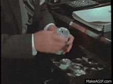 a man in a suit and tie is drinking a can of beer while sitting at a desk .