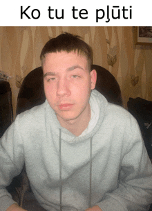 a man in a grey sweatshirt is sitting in a chair with the words ko tu te pluti above him