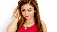 a woman wearing a red top and a necklace is touching her hair
