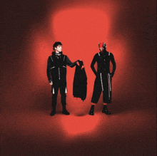 two men are standing in front of a red background and one is holding a black jacket