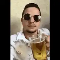 a man wearing sunglasses is holding a glass of beer in his hand .