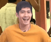 a man in a yellow t-shirt is smiling and laughing in a room .