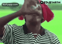 a man in a striped shirt and a red hat is covering his ears with his hand .