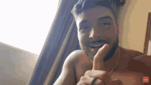 a shirtless man with a beard is giving a thumbs up in front of a window