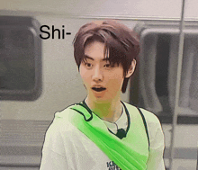 a young man with a green scarf around his neck is standing in front of a train with the word shi above him