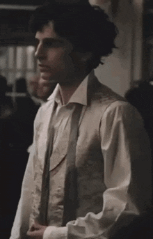 a man wearing a white shirt and a grey vest is standing in a room .