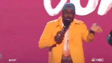 a man in a yellow jacket is holding a microphone in front of a pink background with nbc written on it