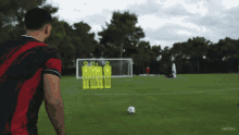 a man in a red and black jersey stands on a soccer field looking at a soccer ball