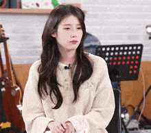 a woman wearing a white sweater is sitting in front of a music stand