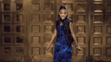 a girl in a blue jumpsuit and black vest stands in front of a gold door