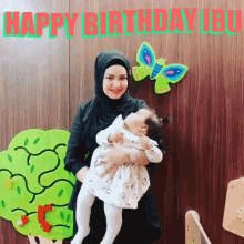 a woman is holding a baby in her arms with the words happy birthday ibu written on the wall behind her