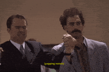 a man in a suit and tie holds another man 's hand and says ' yapping noises ' on the bottom