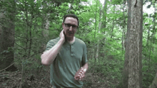 a man in a green shirt talking on a cell phone in the woods