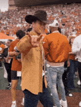 a man wearing a cowboy hat and a tan shirt giving a peace sign