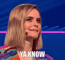 a woman is talking into a microphone on a stage and the words ya know are on the screen .