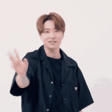 a young man wearing a black shirt and a black t-shirt is waving his hand .