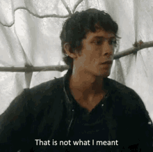 a man in a black jacket is standing in front of a white curtain and says `` that is not what i meant '' .