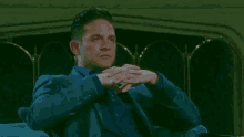 a man in a suit and blue shirt sits with his hands folded