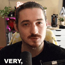 a man with a mustache is sitting in front of a microphone and the word very is on the bottom