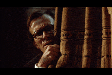 a man wearing glasses is peeking out from behind a curtain