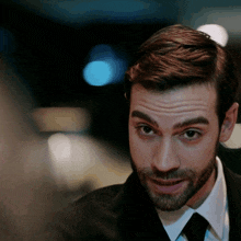 a man with a beard wearing a suit and tie looks at the camera