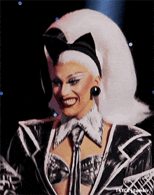a woman with white hair and a black and white outfit is smiling for the camera ..