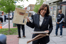 a woman in a black suit is holding a piece of paper with a picture of a man in a room on it