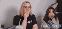two women are laughing in front of a microphone and the words dark web are visible