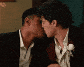 a man in a suit kisses another man in a white shirt