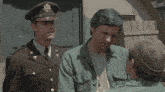a man in a us army uniform talks to another man in a green shirt