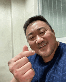 a man in a blue shirt is making a heart shape with his hand