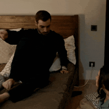 a man in a black sweater sits on a bed